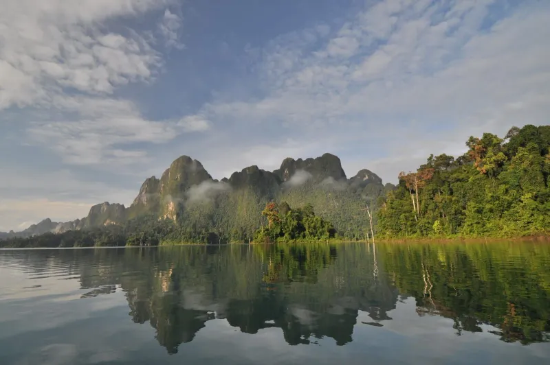Bright daytime view across Cheow Lan Lake toward limestone mountains in Khao Sok park