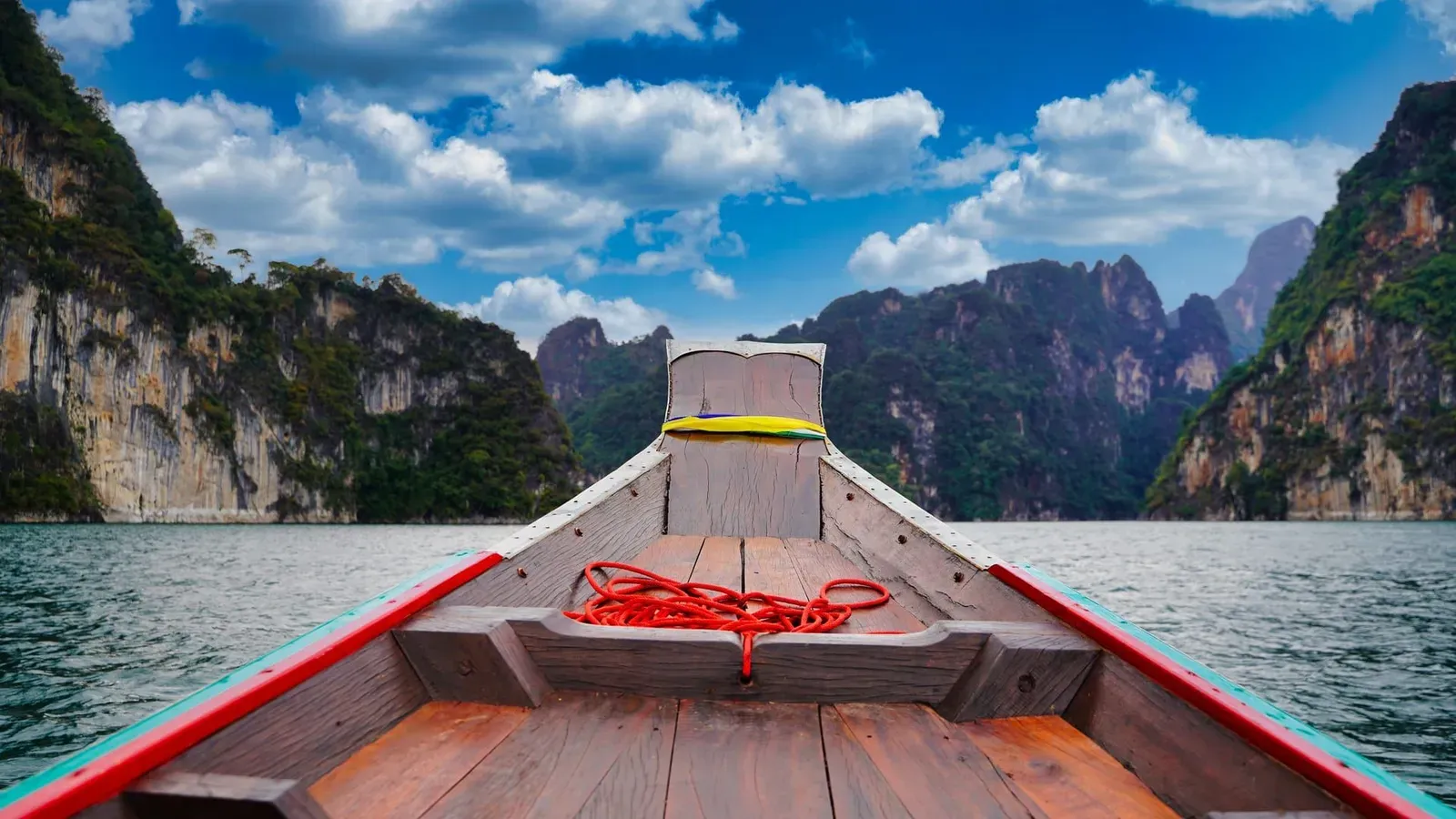 Longtail boat passing towering limestone cliffs on Cheow Lan Lake near Khao Sok National Park