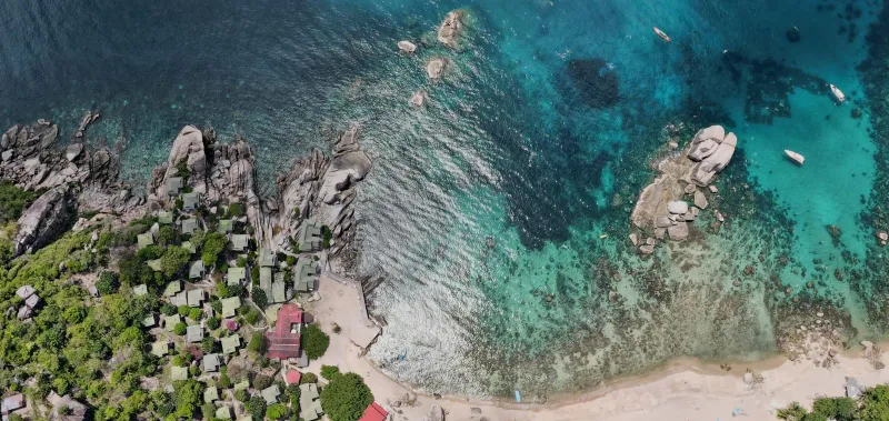 Coastal village nestled against turquoise waters and rocky shoreline near Koh Tao Koh Samui route