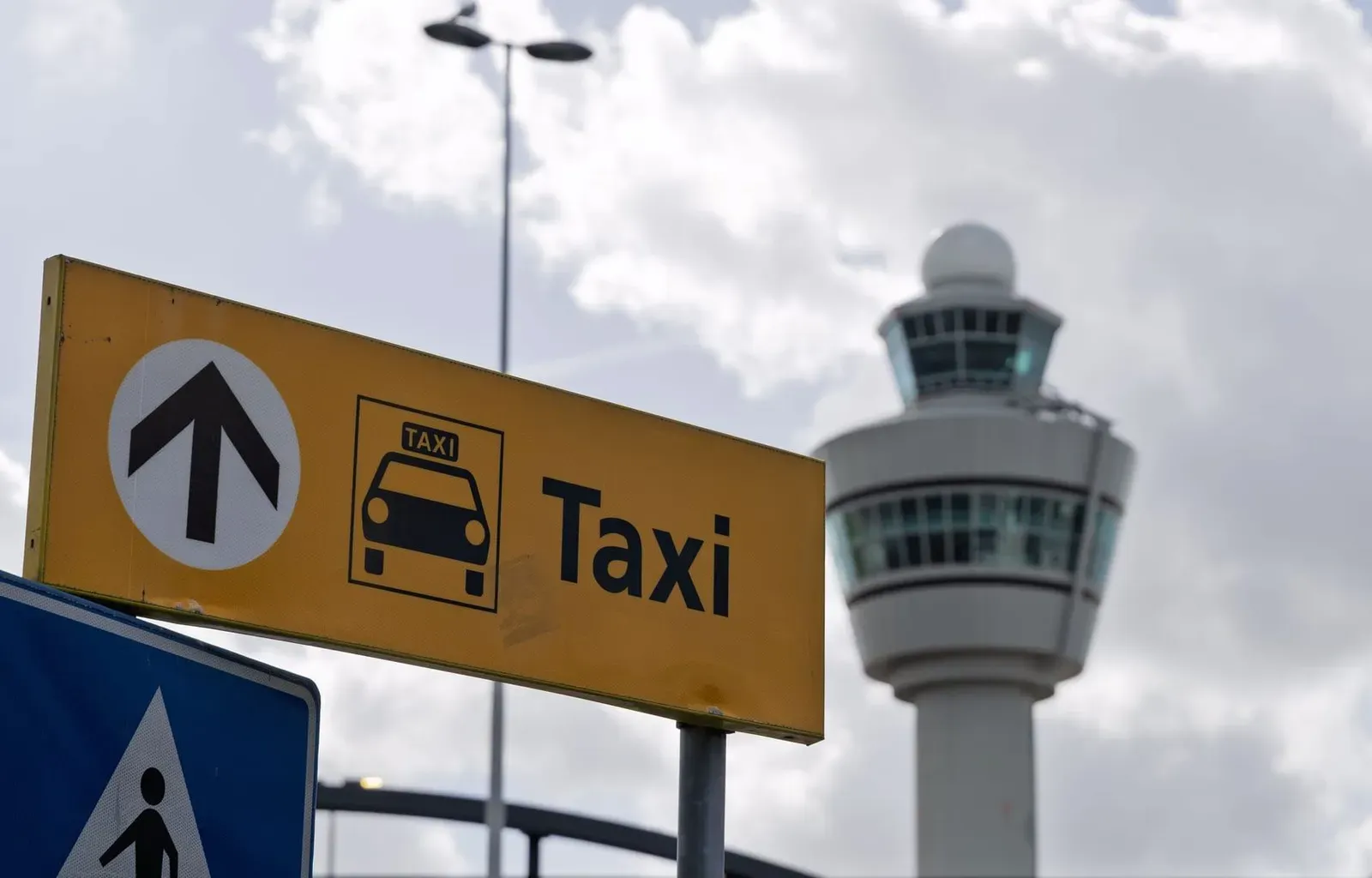 Taxi sign at Koh Samui Airport with the control tower visible against a cloudy sky