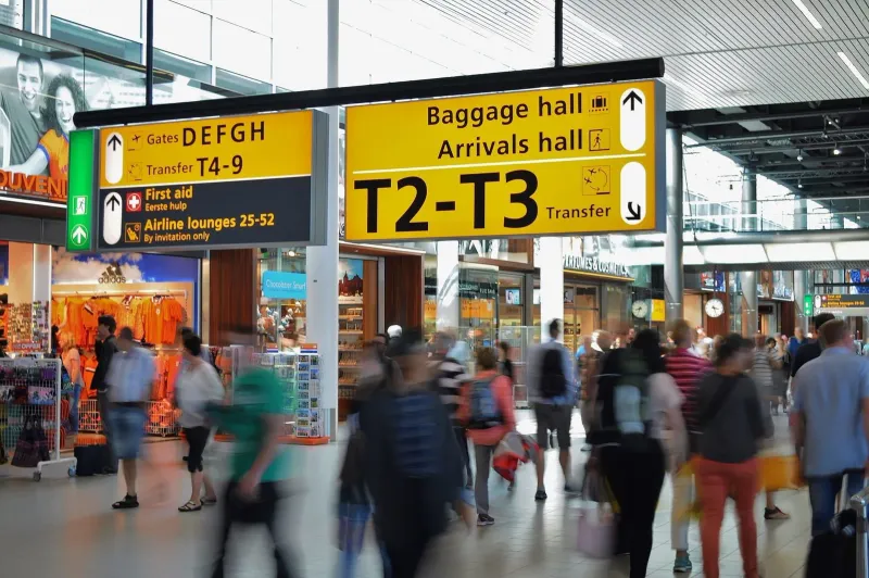 Crowded arrivals hall with signage guiding passengers toward baggage claim and transport