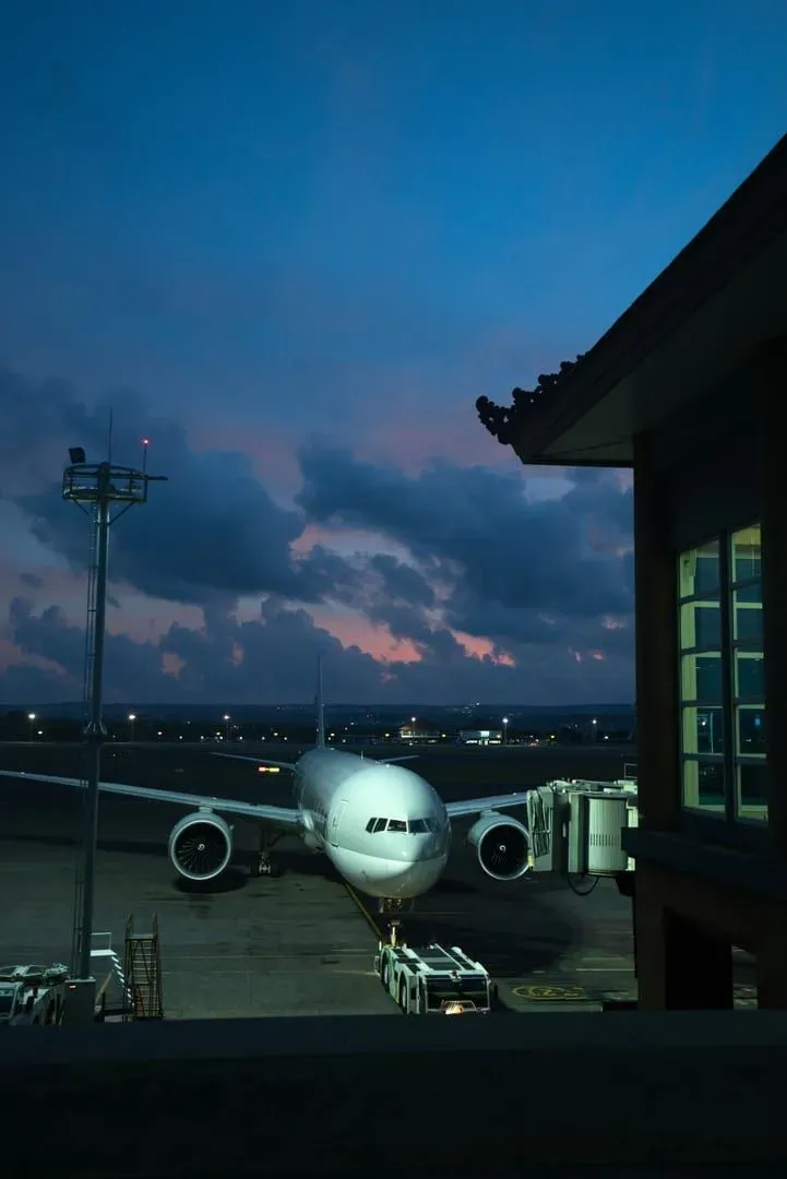 Aircraft parked at an airport at dusk beside a traditional Thai-style building silhouette