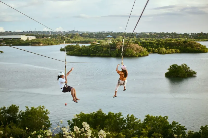 Due persone in zipline sopra acque calme in un parco avventura nella giungla simile a quelli di Koh Samui