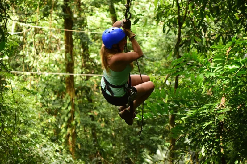 Donna in zipline che attraversa la fitta volta verde di una foresta, simile ai parchi di zipline nella giungla di Koh Samui