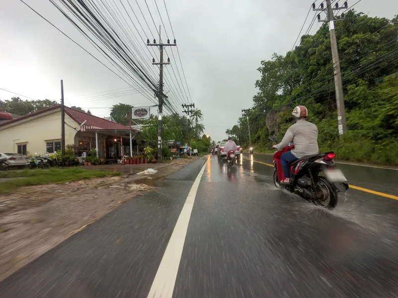 Route 4169 near Lamai in the rain, a motorbike passing shopfronts and a red-roofed building