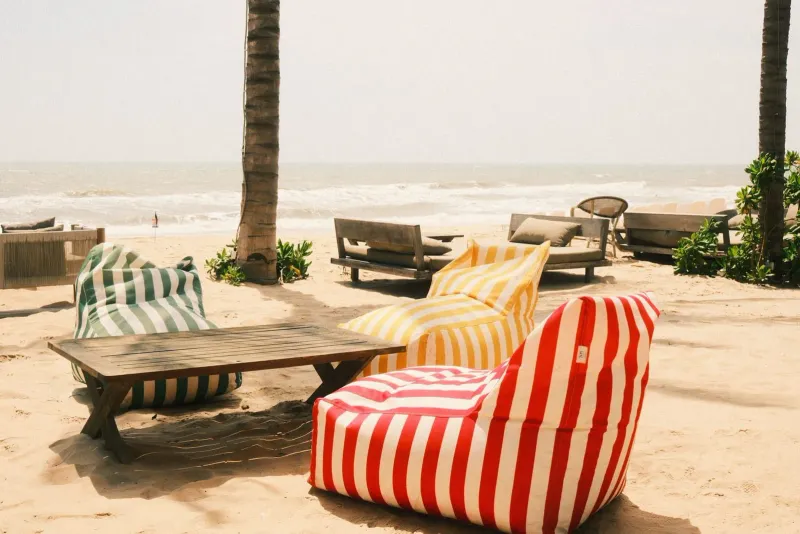 Colorful bean bag chairs arranged on sand beside the sea, typical beach club seating