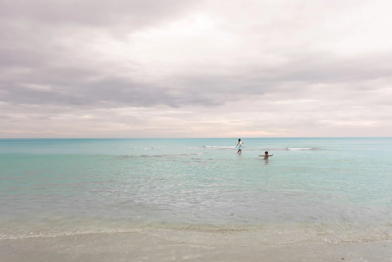 Children playing on a quiet beach under a cloudy sky, similar to Koh Samui's calmer coasts