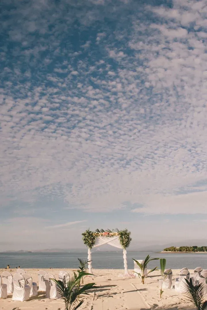 Beach wedding setup with a floral arch and white chairs on a tropical shoreline