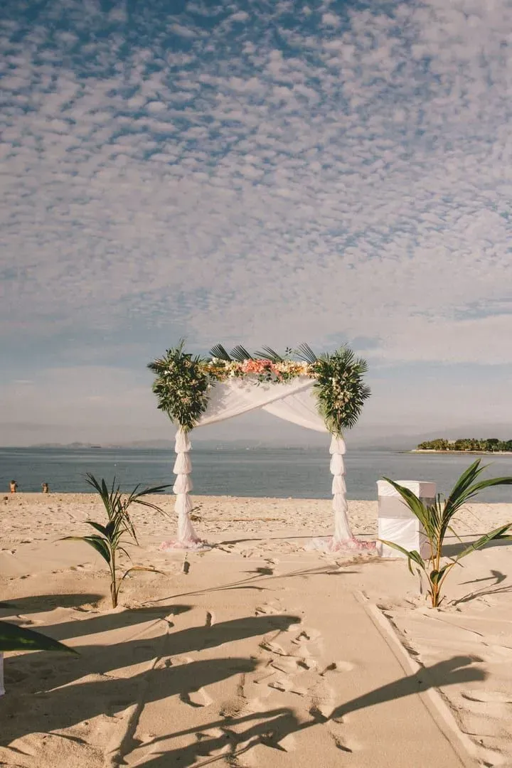Elegant wedding arch on a sandy tropical beach framed by ocean and open sky