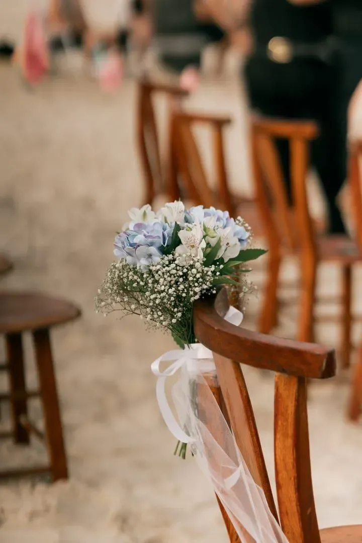 Floral arrangement tied to a wooden chair as part of a beach wedding decor setup