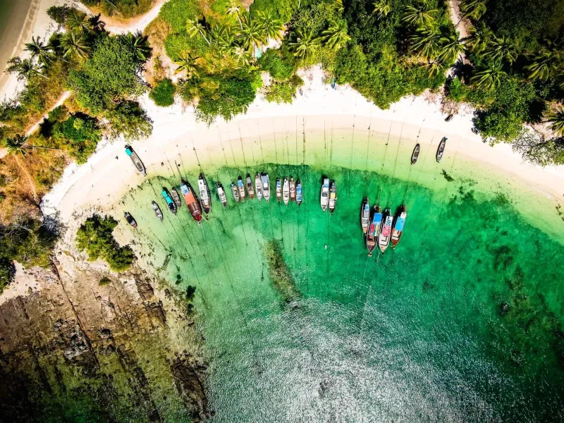 Longtail boats along a tropical beach with turquoise water and greenery