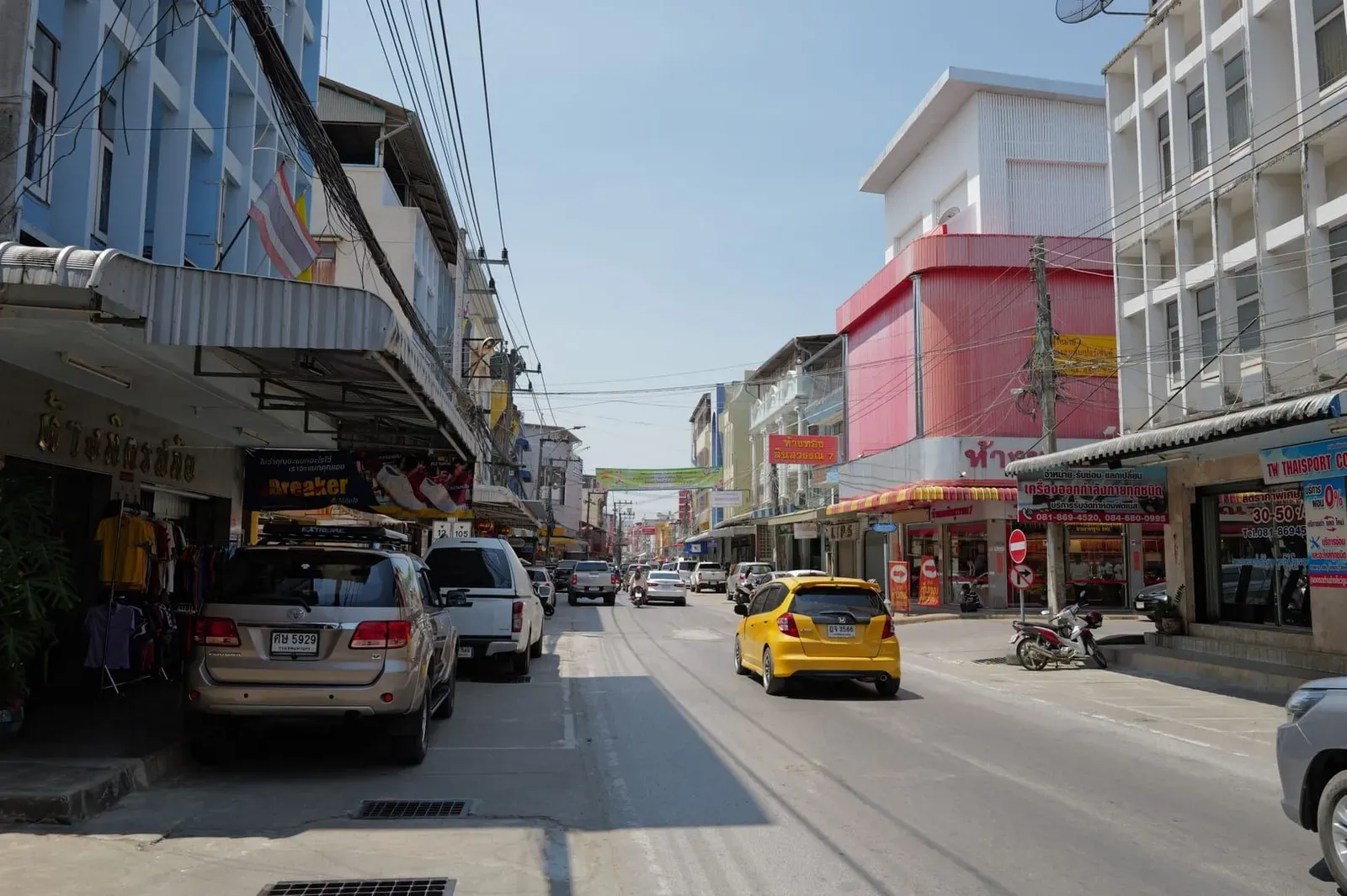 Traffic and colorful storefronts on a Koh Samui town street where local car rental shops operate