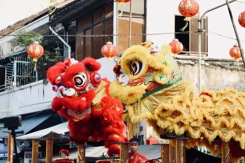 Lion dance performers in red and yellow costumes with traditional lanterns