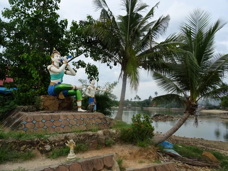 Painted Thai mythological statues under a coconut palm near a lagoon on Koh Samui, close to the Big Buddha temple complex