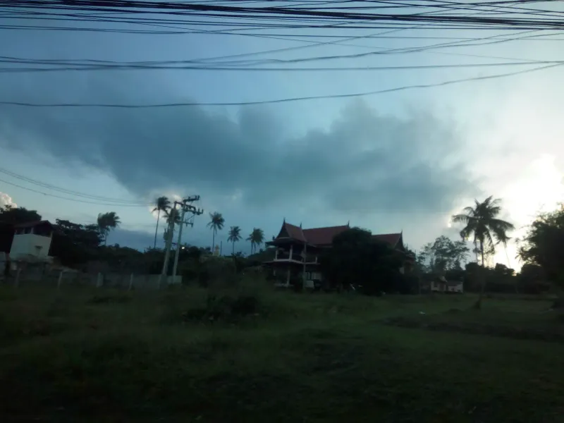 Dusk view of a traditional Thai-roofed building and coconut palms in a village near Choeng Mon, Koh Samui