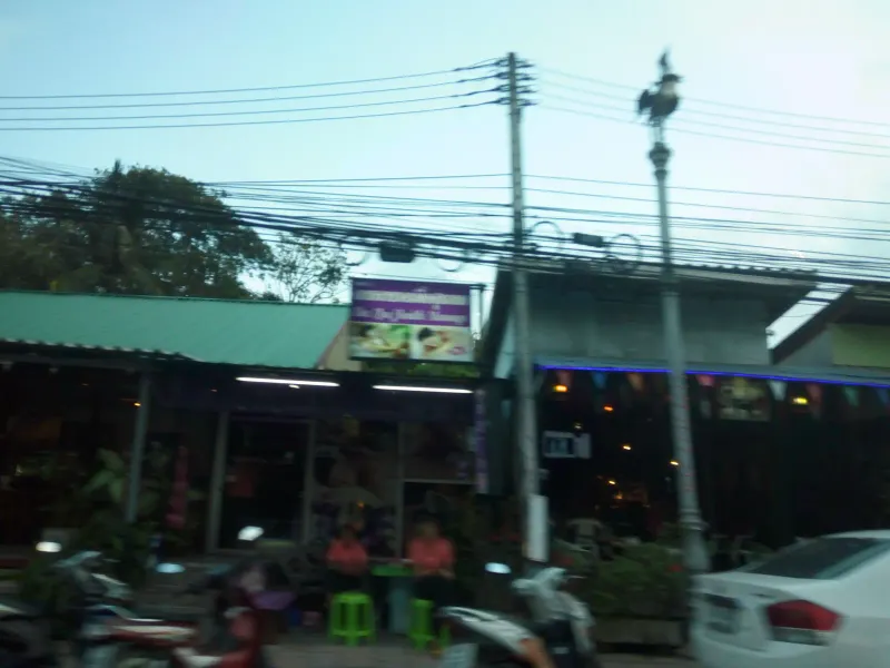 Massage shop and small restaurant signboards lit up at dusk on the village road behind Choeng Mon Beach, Koh Samui