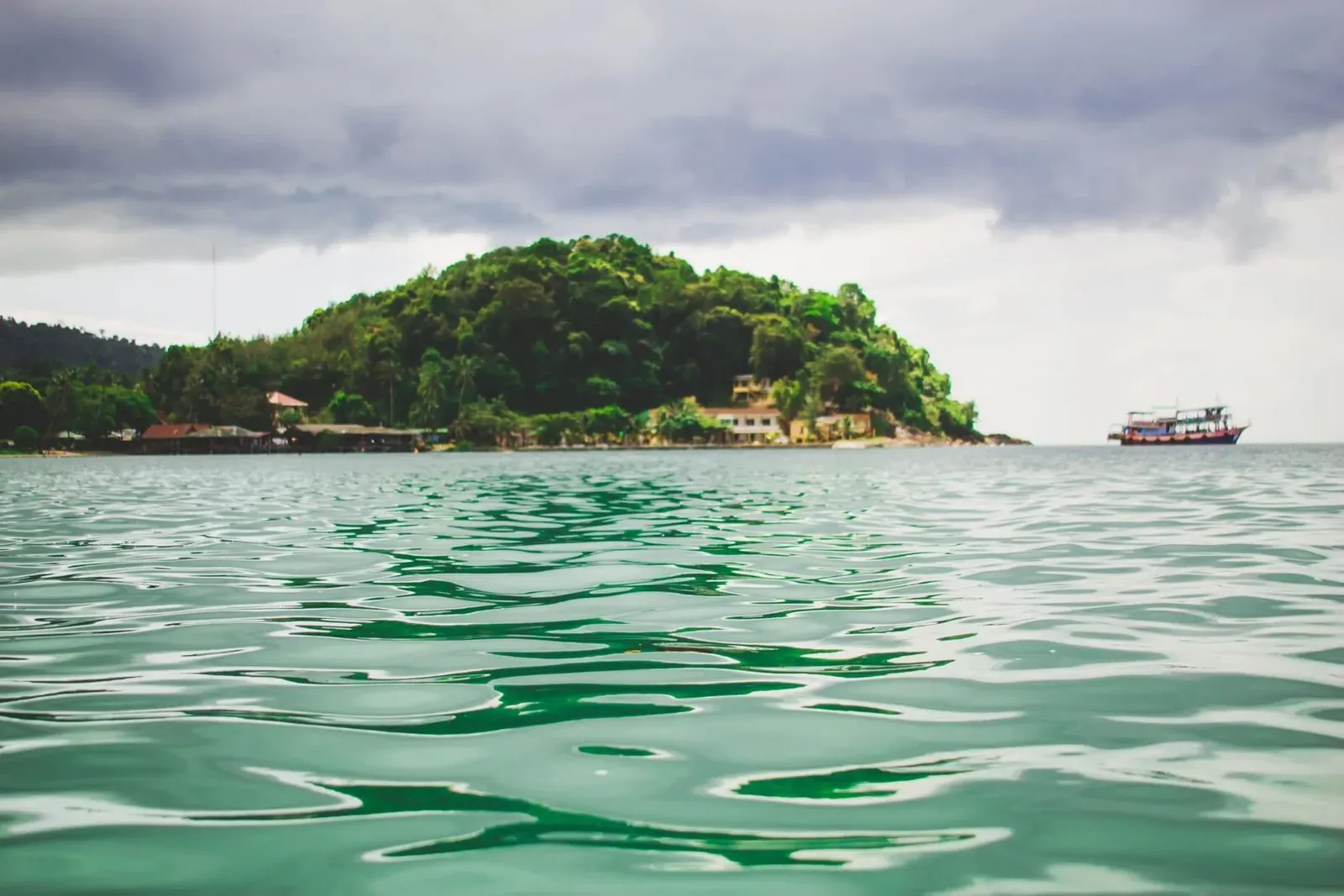 Lush green island surrounded by clear turquoise water with a boat passing nearby, similar to Koh Tan's coastline