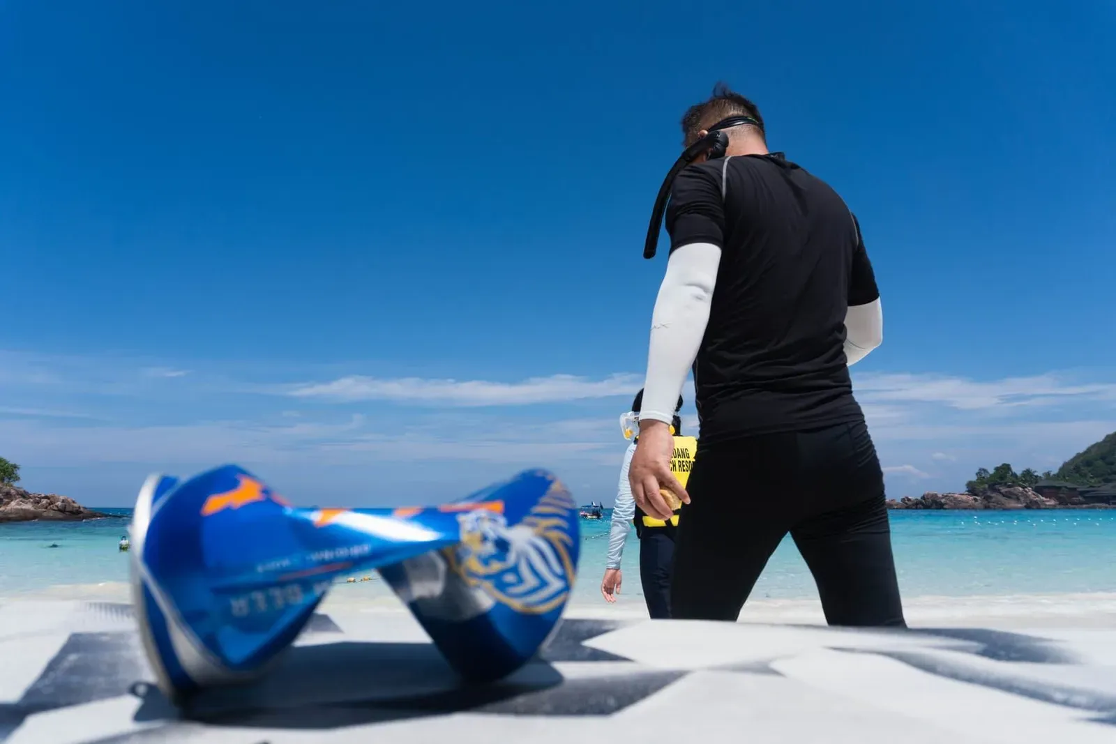 Snorkeler wearing a rash guard walking into the sea on a Koh Samui beach with gear in hand