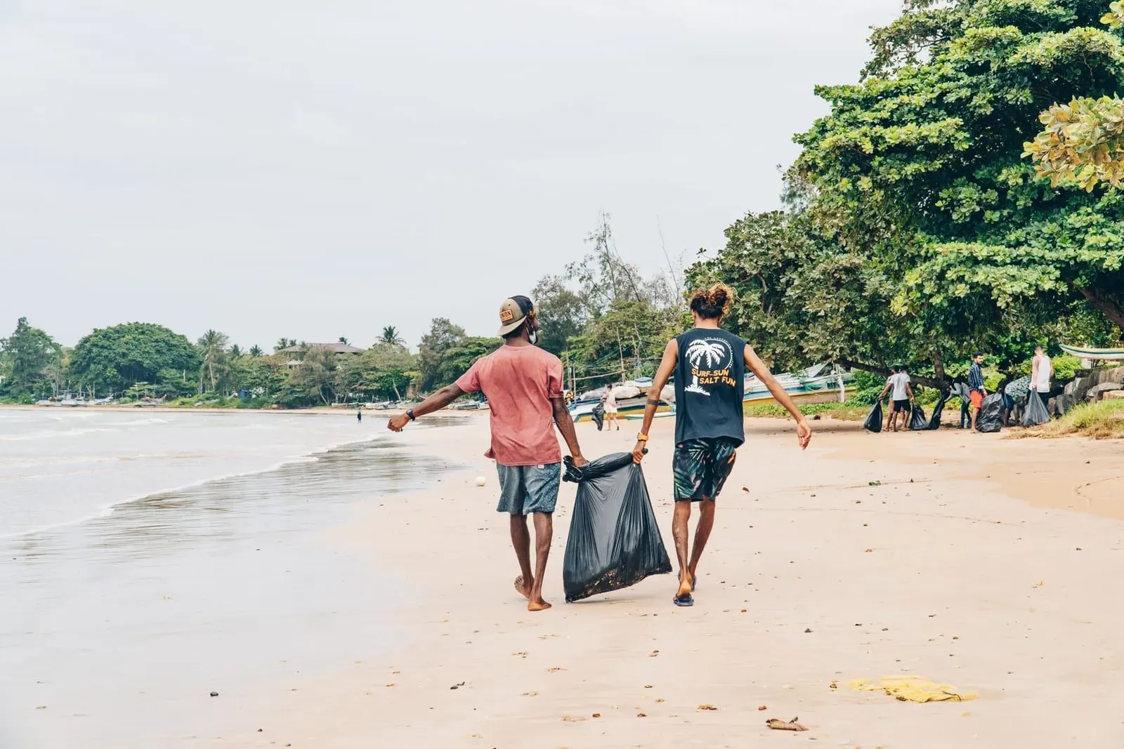 Volunteers carrying trash bags along a beach shoreline as part of a community cleanup