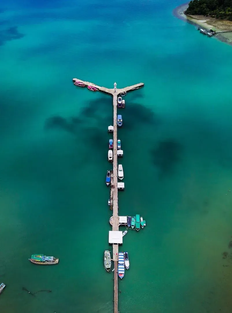 Aerial view of a pier with moored boats in clear turquoise coastal water in Thailand