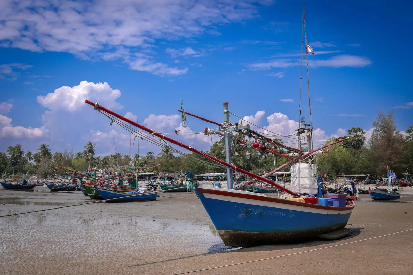 Colorful traditional fishing boats resting on the sandy shore at low tide in coastal Thailand