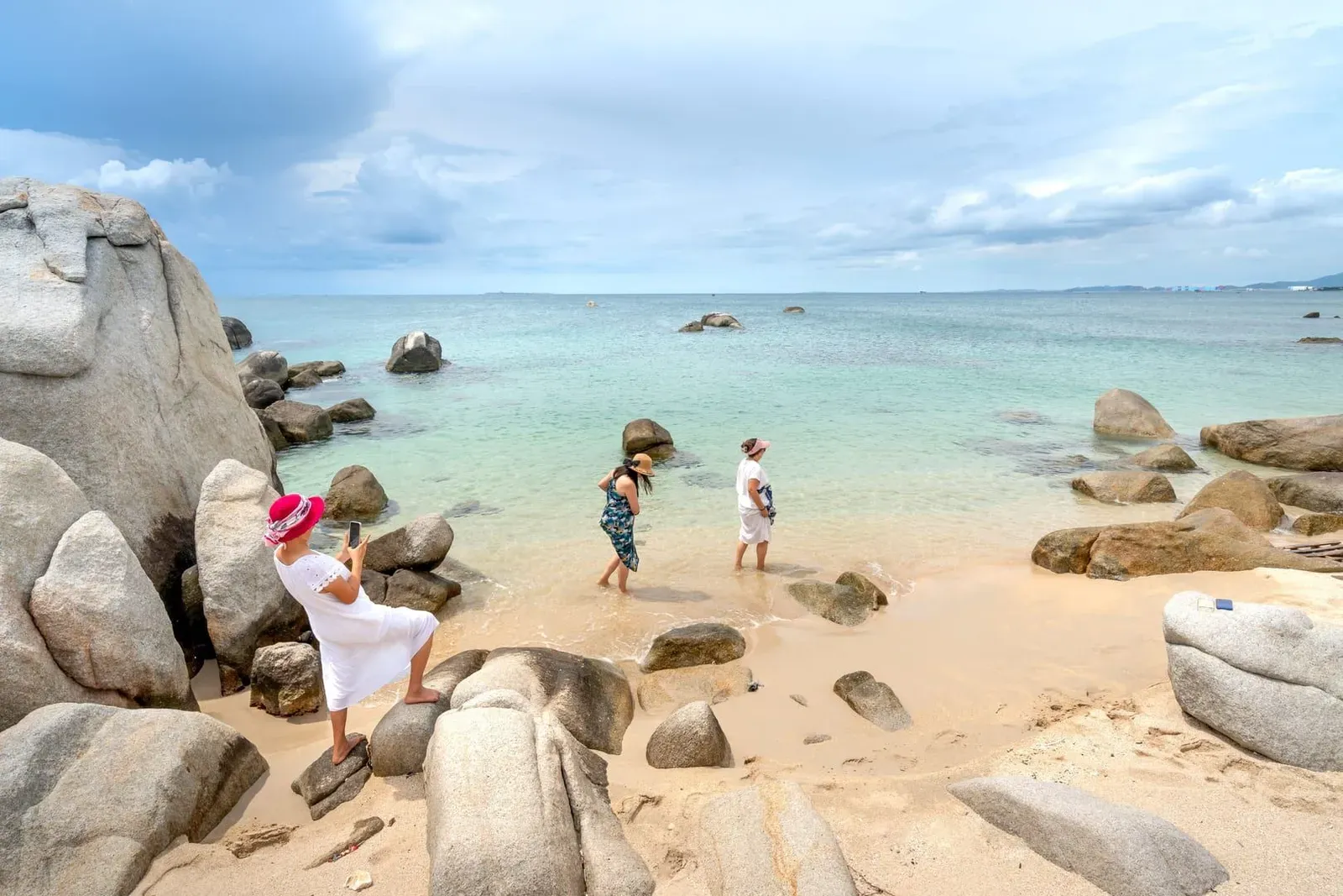 Travelers exploring a rocky Koh Samui beach, a reminder to check tide and currency needs
