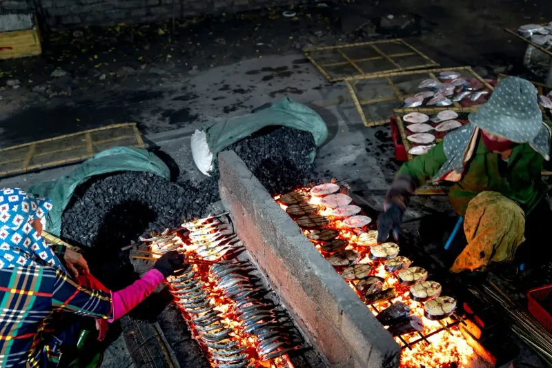 Local vendors grilling whole fish over an open flame at an outdoor Koh Samui stall
