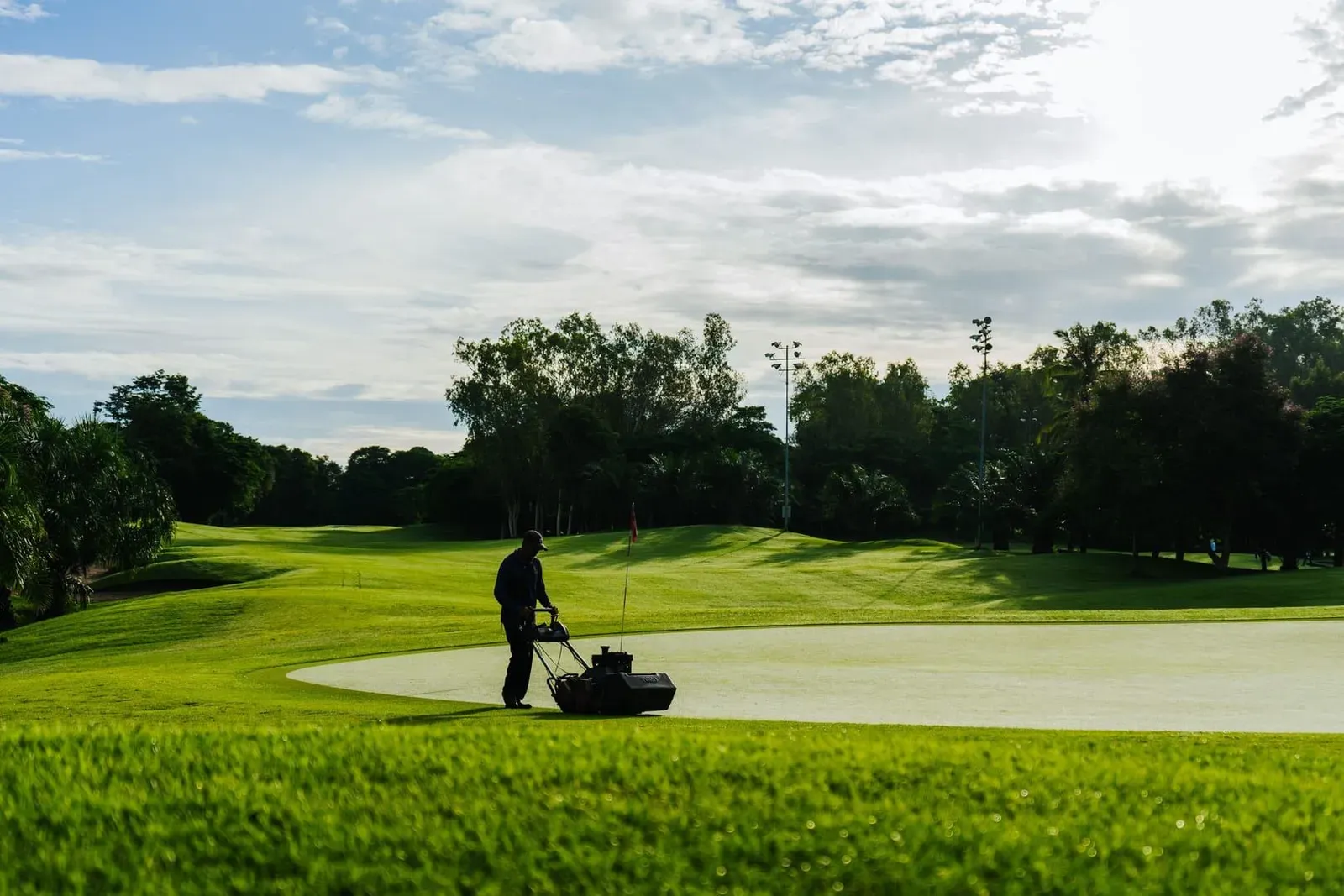 Groundskeeper mowing the green on a tropical golf course similar to Santiburi Samui Country Club