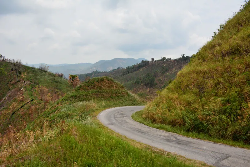 Route de bitume étroite et sinueuse montant entre des collines herbeuses en Thaïlande