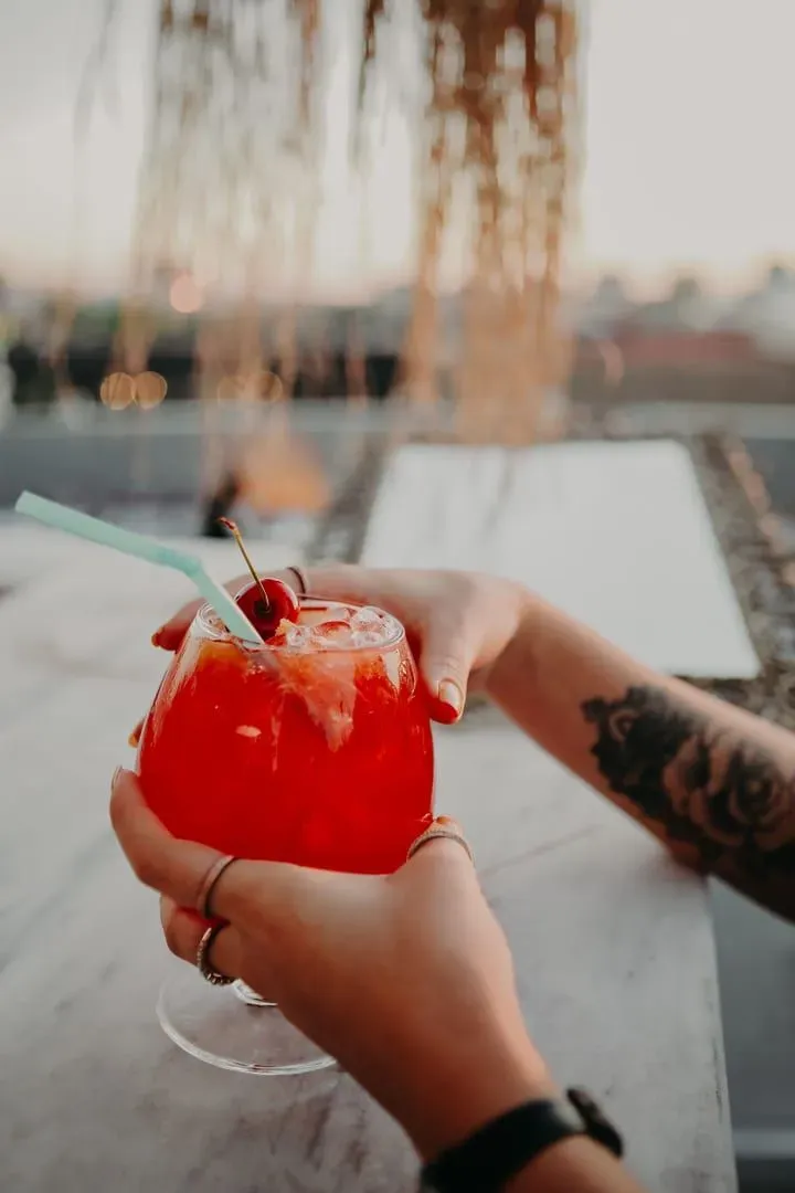 Hand holding a garnished cocktail against a rooftop bar sunset backdrop on Koh Samui