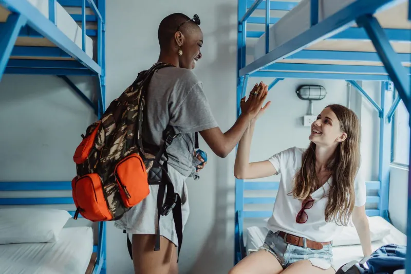 Two hostel guests high-fiving in a bright Koh Samui dorm room during a budget stay