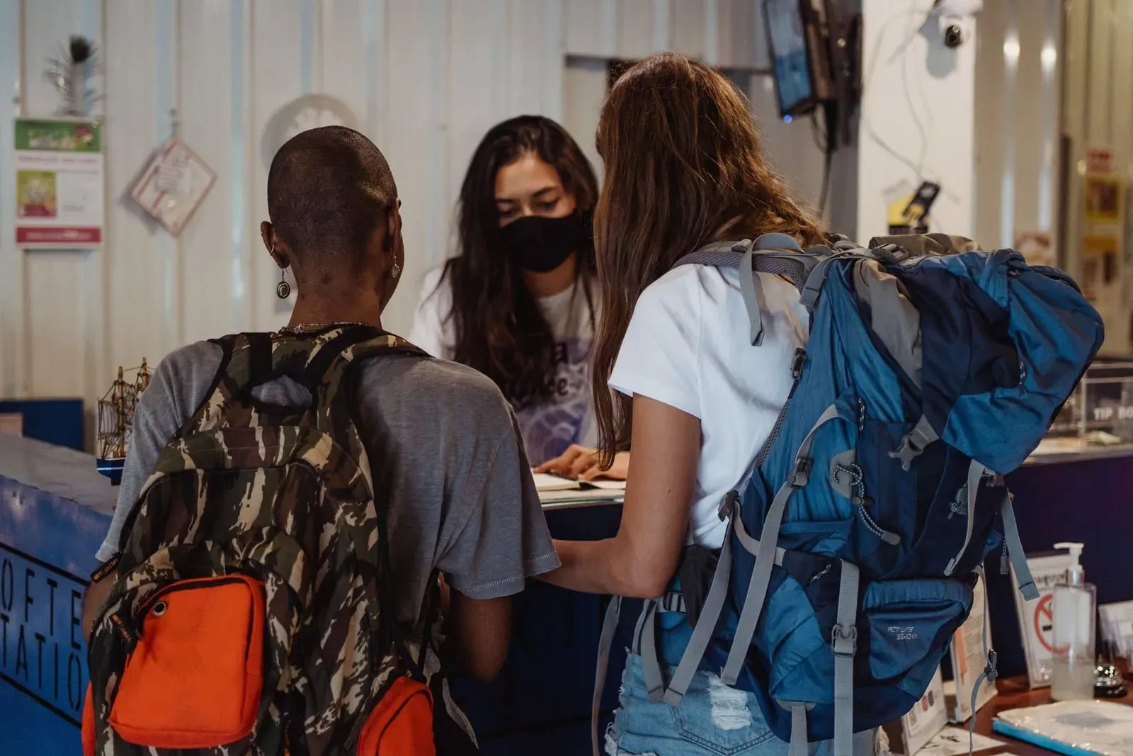 Two backpackers checking in at a hostel reception desk with their travel bags on Koh Samui