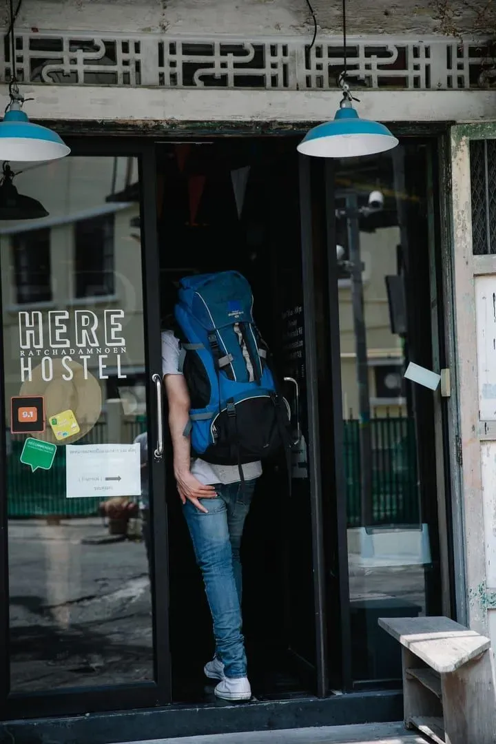 A backpacker with a travel bag entering a hostel building on a budget trip to Koh Samui