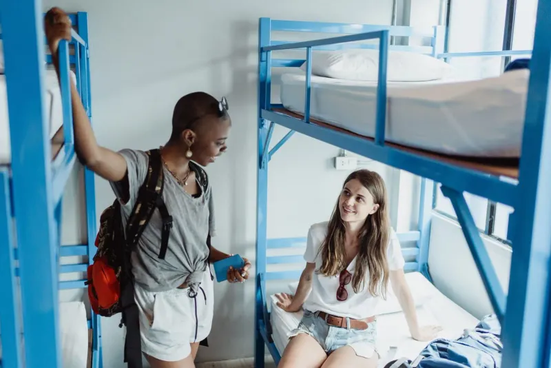 Two young travelers talking in a Koh Samui budget hostel room with bunk beds