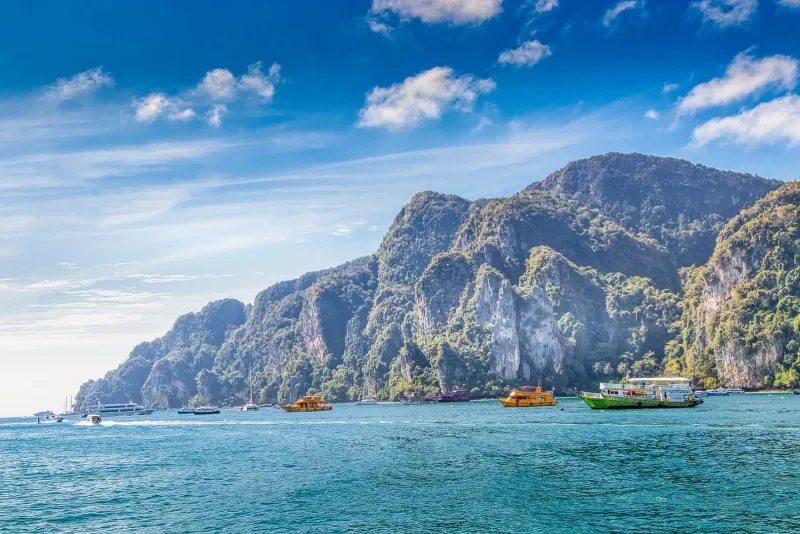 Colorful boats and clear water at a limestone island stop on a Gulf of Thailand day trip