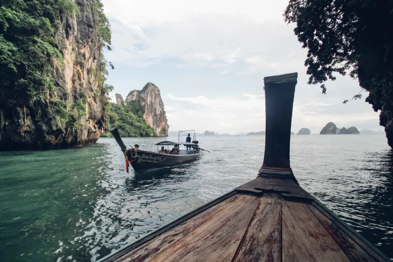 Passengers riding a traditional longtail boat past towering limestone cliffs on a Thailand island tour