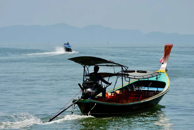 Silhouette of a longtail boat operator navigating calm water with distant islands in view
