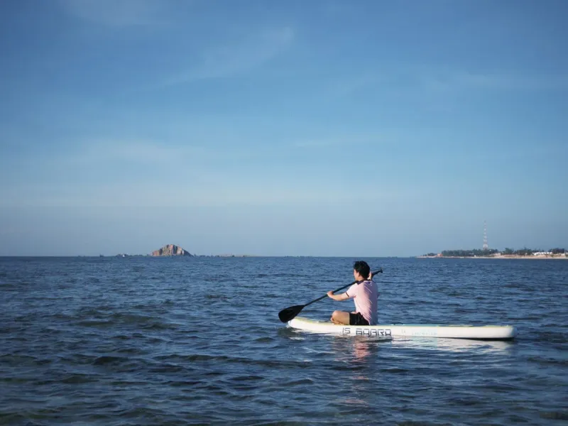 Person paddleboarding alone on calm, sunlit open water
