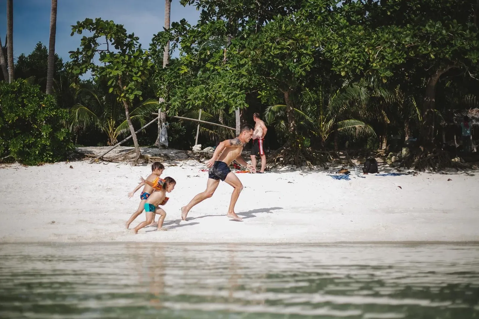 Father and two kids playing together on a calm Koh Samui beach in the afternoon sun