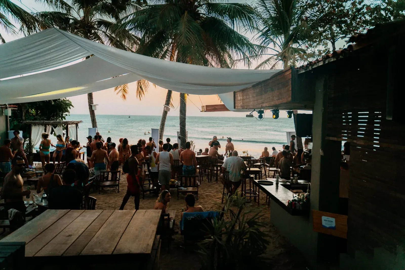 Vibrant beachside bar scene with people relaxing under palm trees at sunset in Chaweng Koh Samui