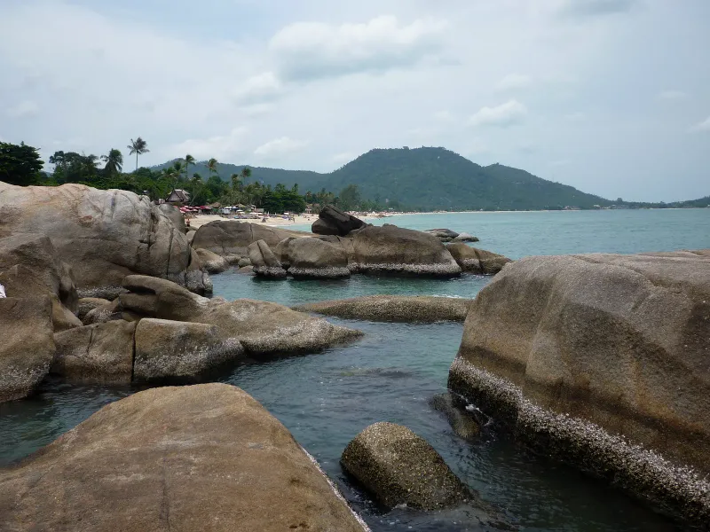 Wide view of Lamai Beach's rocky boulder coastline with palm trees and hills, Koh Samui