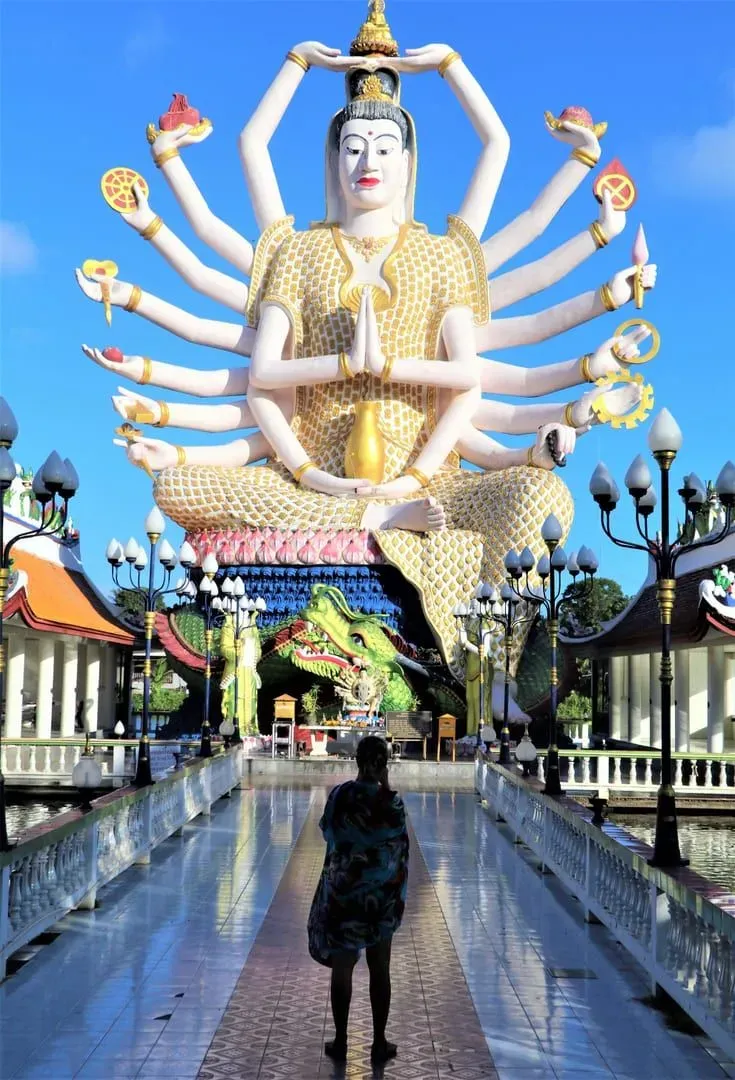 Visitor standing quietly before a multi-armed deity statue inside a Koh Samui temple hall