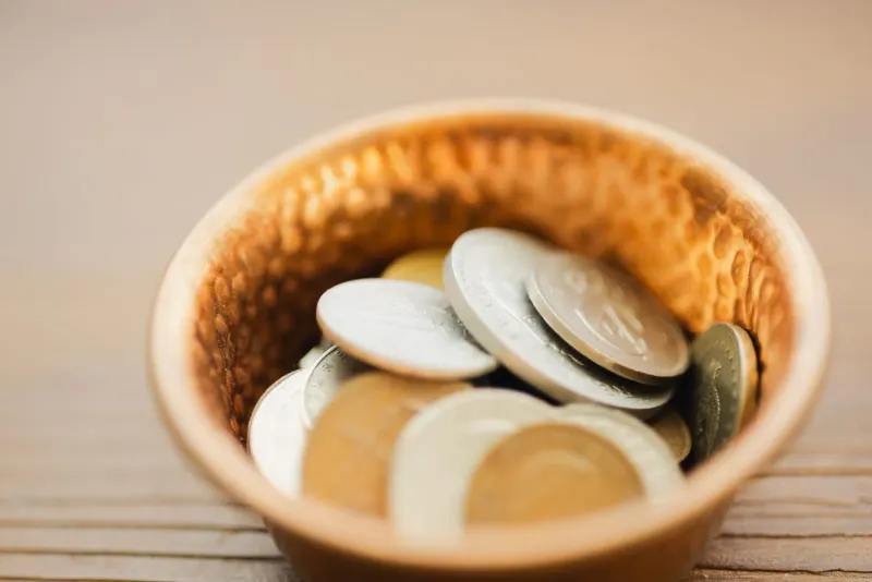Close-up of coins in a metal bowl representing small daily expenses on a Koh Samui budget
