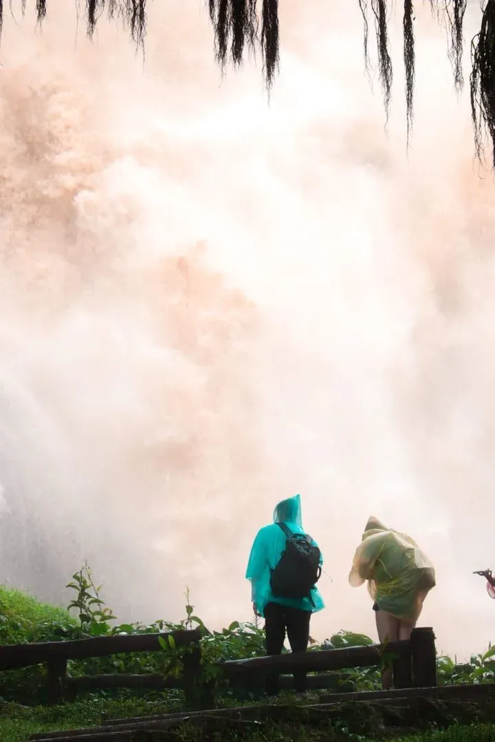 Two hikers in raincoats standing beside a misty waterfall, illustrating wet-weather hiking conditions on Koh Samui in November