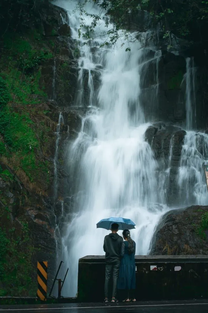 Couple sheltering under an umbrella while admiring a jungle waterfall during Koh Samui's wet season