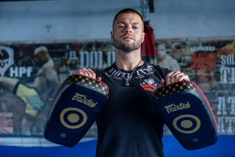 Muscular boxer holding muay thai pads inside a Koh Samui training camp