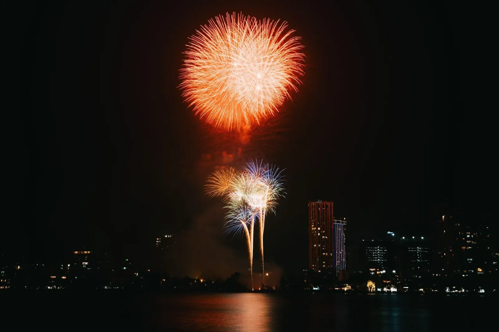 Fireworks reflecting off calm water near a beachfront skyline during a Koh Samui New Year celebration