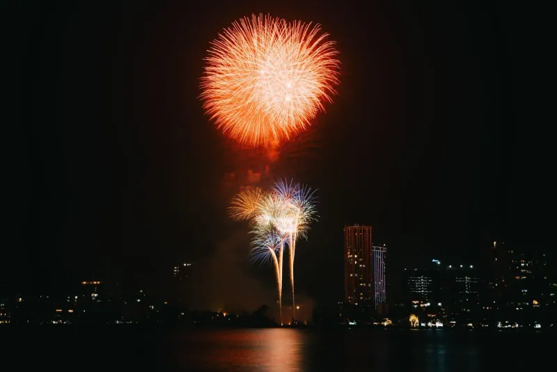 Fuochi d'artificio che si riflettono sull'acqua calma davanti allo skyline di un lungomare durante i festeggiamenti di Capodanno a Koh Samui