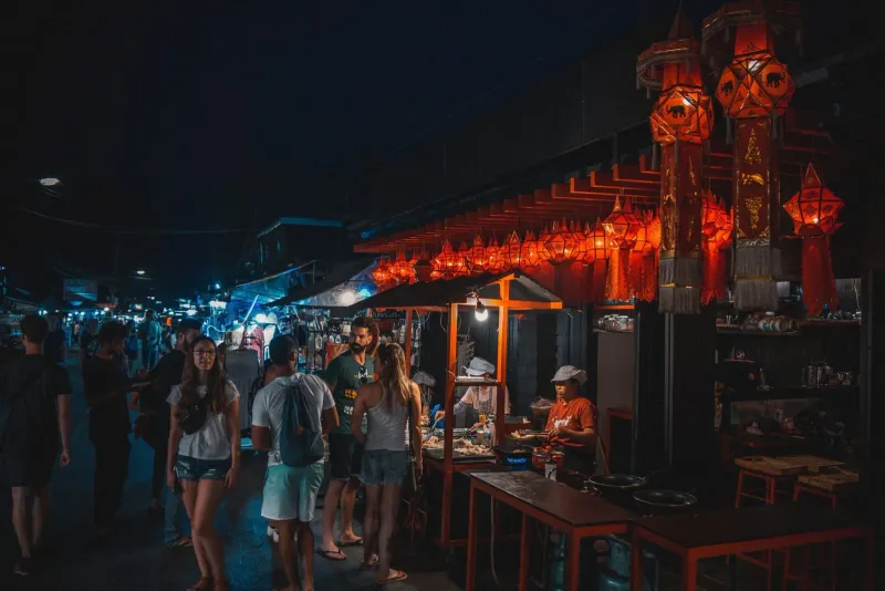 Tourists and vendors walking through a lantern-lit walking street market in the evening