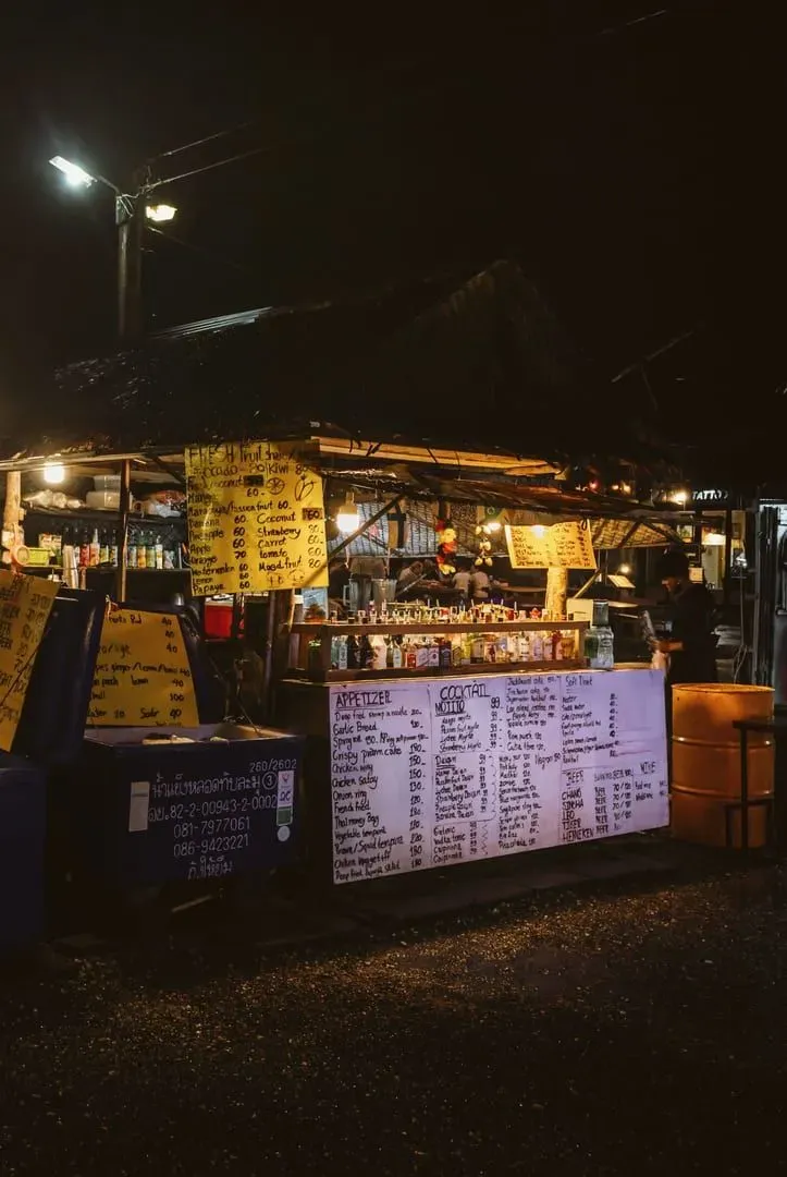 Bright market stalls selling Thai street food with vibrant lights along a busy walkway